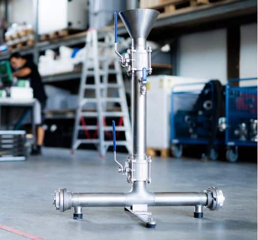 Eine metallene Industriemaschine mit Trichterdeckel, die auf einer Fabriketage inmitten von Werkzeugen und Geräten steht, verkörpert die Präzision moderner Industriepraktiken.